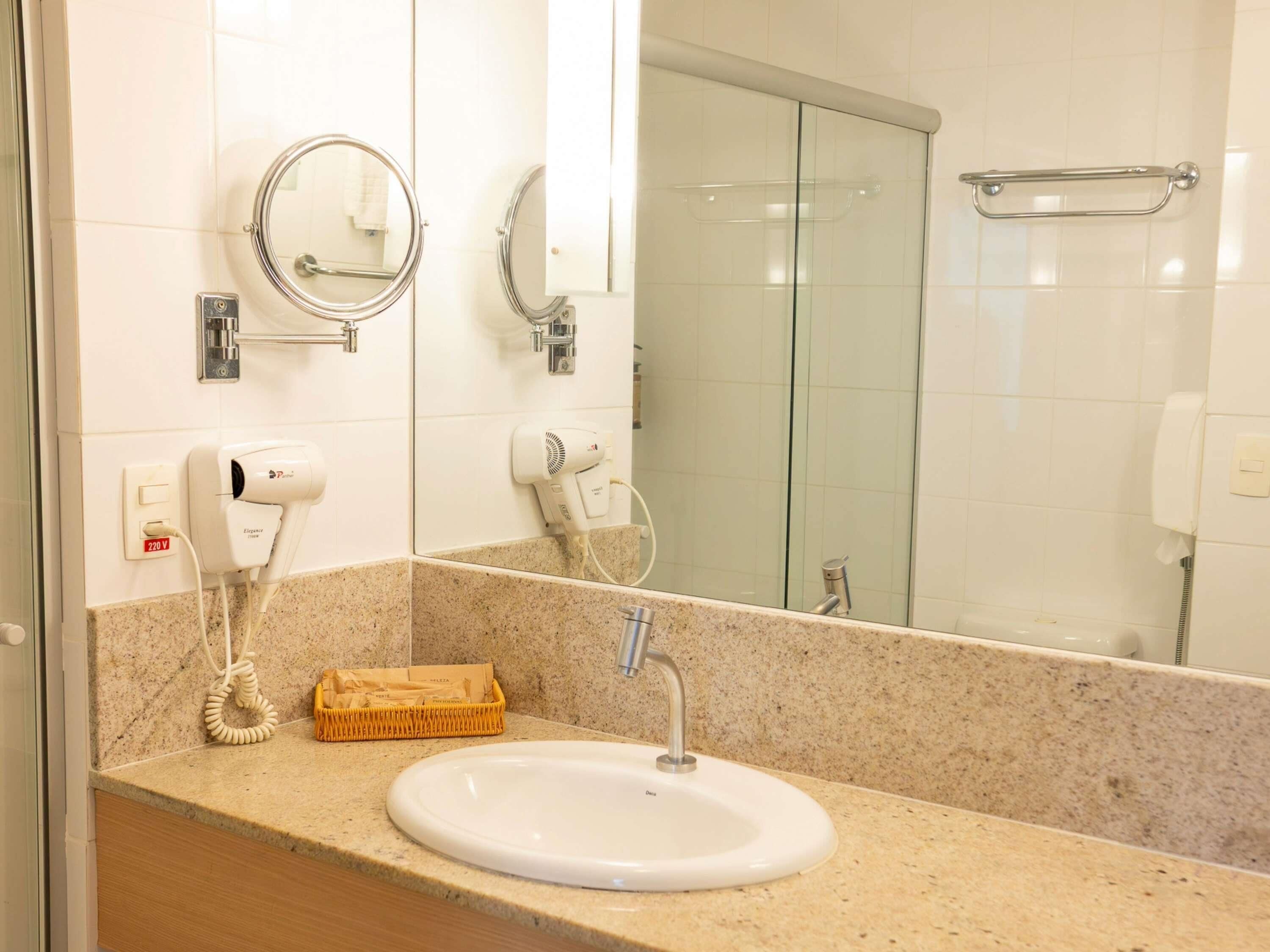 A bathroom with a sink, two mirrors, a hairdryer, a towel rack, and a glass shower enclosure.