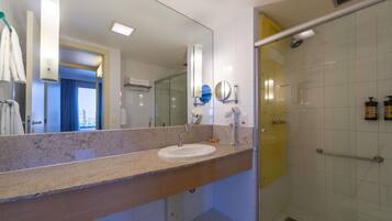 Un baño moderno con encimera de granito, un lavamanos, un espejo, un secador de pelo de mano y una ducha con mampara de vidrio.