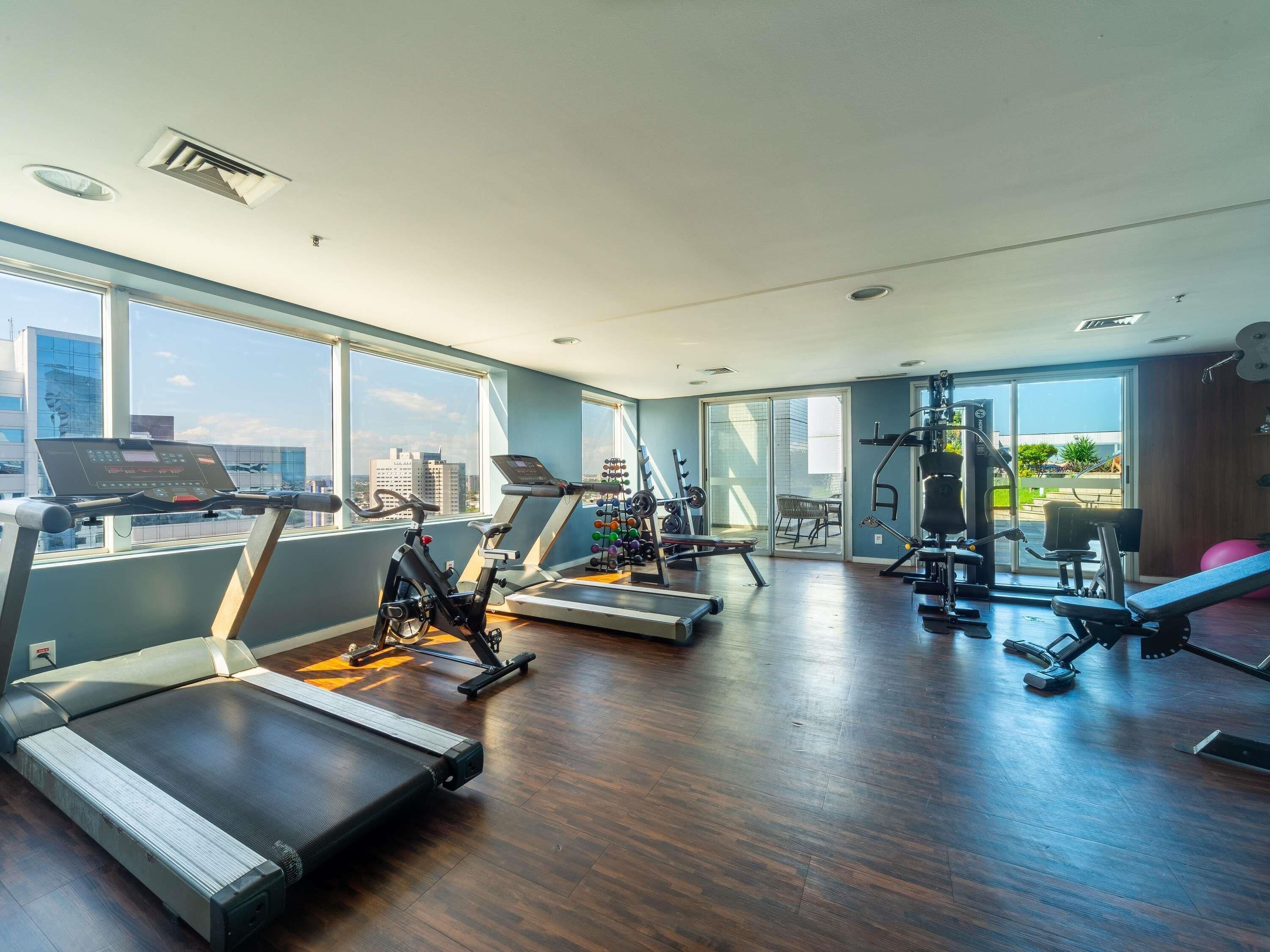 Un gimnasio amplio con cintas de correr, elípticas y equipo de levantamiento de pesas. Amplias ventanas ofrecen vistas de la ciudad.
