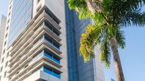 A modern hotel with a glass facade, a palm tree in the foreground, and a clear blue sky. - Mercure Manaus Hotel (Manaus)