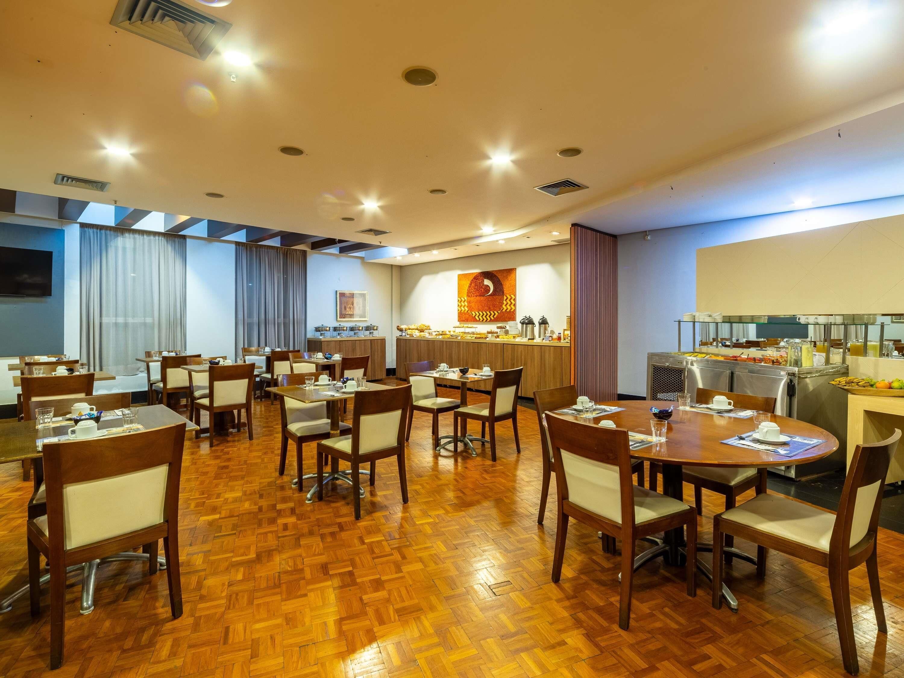 A hotel dining area with multiple tables and chairs, a buffet counter, and a kitchen area.