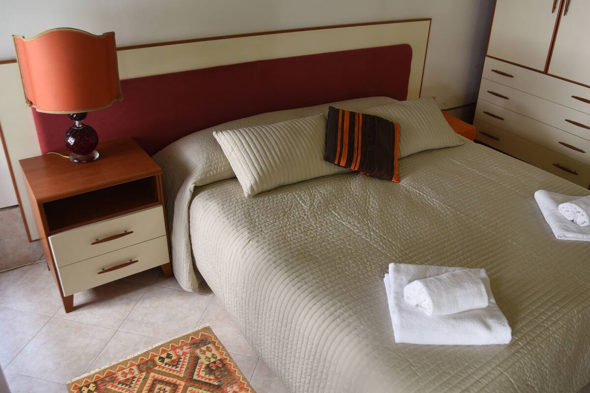 A neatly made bed with two pillows, a bedside table with a lamp, and a wardrobe.
