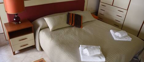 A neatly made bed with two pillows, a bedside table with a lamp, and a wardrobe.