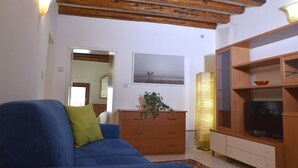 Een woonkamer met een blauwe bank, houten kasten, een televisie en een plant.