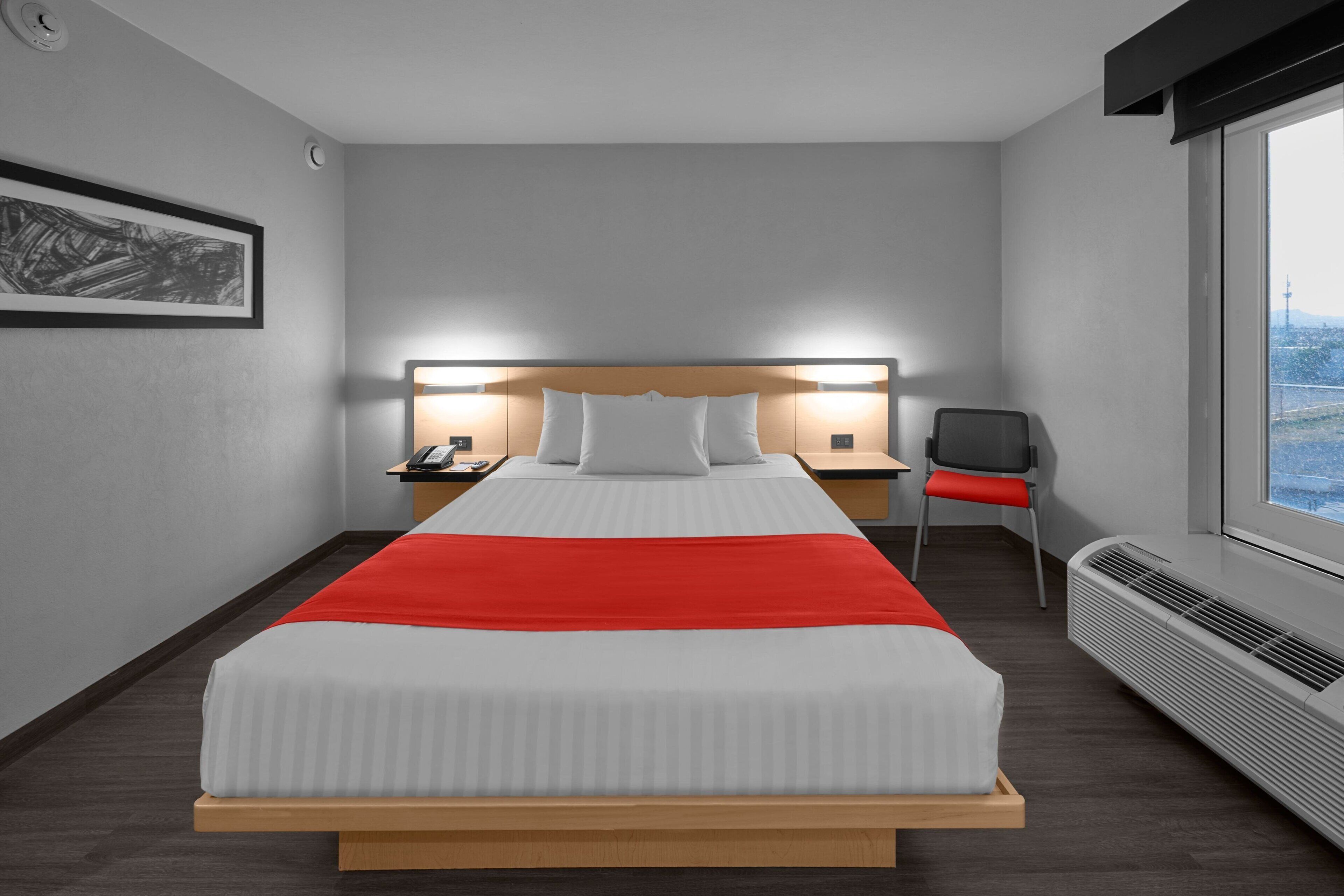 Une chambre d’hôtel avec un lit, des tables de chevet, une chaise et une fenêtre donnant sur un paysage agréable.