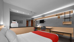 Una habitación de hotel moderna con una cama grande, un escritorio, una silla, un televisor y una kitchenette pequeña.