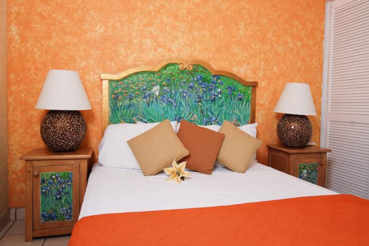 Une chambre à coucher comprenant un lit, deux tables de chevet et une tête de lit ornée d’un motif floral.