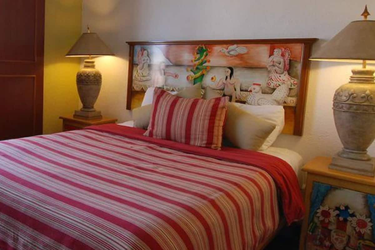 Un lit bien fait, avec une couvre-lit à rayures, deux lampes de chevet et une tête de lit décorative ornée d’un tableau.