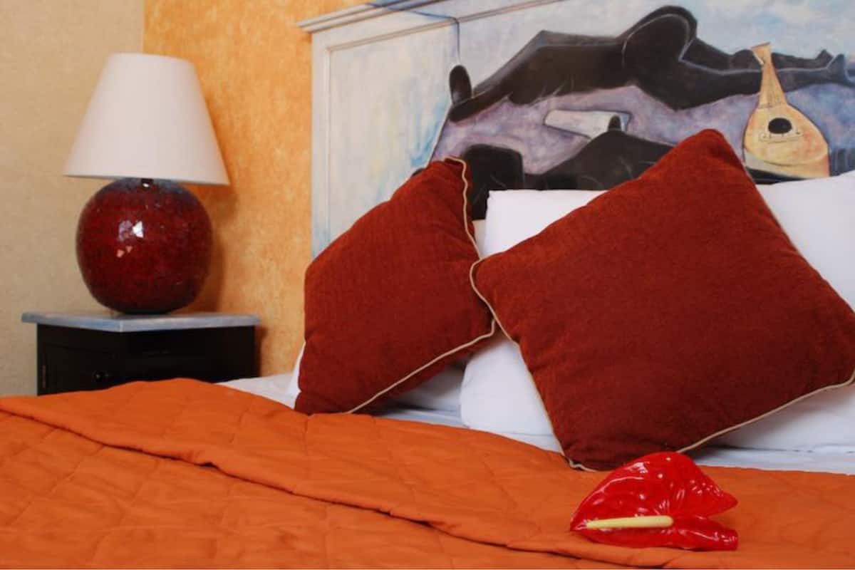 Un lit avec des oreillers rouges, une couverture orange et une lampe rouge posée sur une table de chevet.