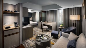 Ein modernes Hotelzimmer mit einer Couch, einem runden Couchtisch, einem Schreibtisch, einem Fernseher und einer Minibar.