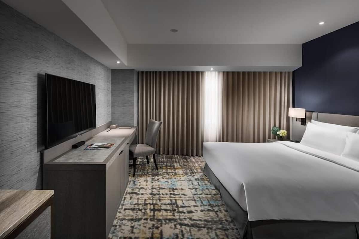 Une chambre d’hôtel moderne dotée d’un grand lit, d’un téléviseur à écran plat fixé au mur, d’un bureau avec une chaise et d’un tapis à motifs.