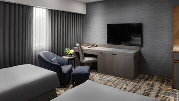 A hotel room with a large bed, a desk with a chair, a television, and a small table with a vase of flowers.