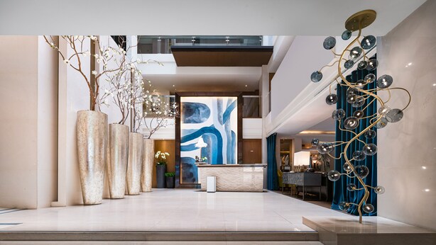 Eine geräumige Lobby mit einer modernen Rezeption, großformatiger abstrakter Kunst an der Wand und dekorativer Beleuchtung.