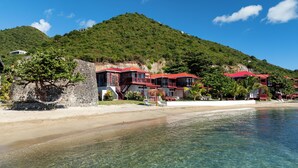 A beachfront hotel with multiple red-roofed buildings, clear waters, and a hillside backdrop. - Fort Recovery Beachfront Resort (West End)