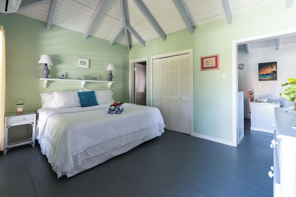 A bedroom with a bed, bedside tables, a nightstand, a dresser, a closet, and a door leading to another room.