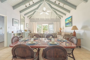 A dining area with a large table set for six, surrounded by wooden chairs, with a ceiling fan above and a painting on the wall. - Fort Recovery Beachfront Resort (West End)
