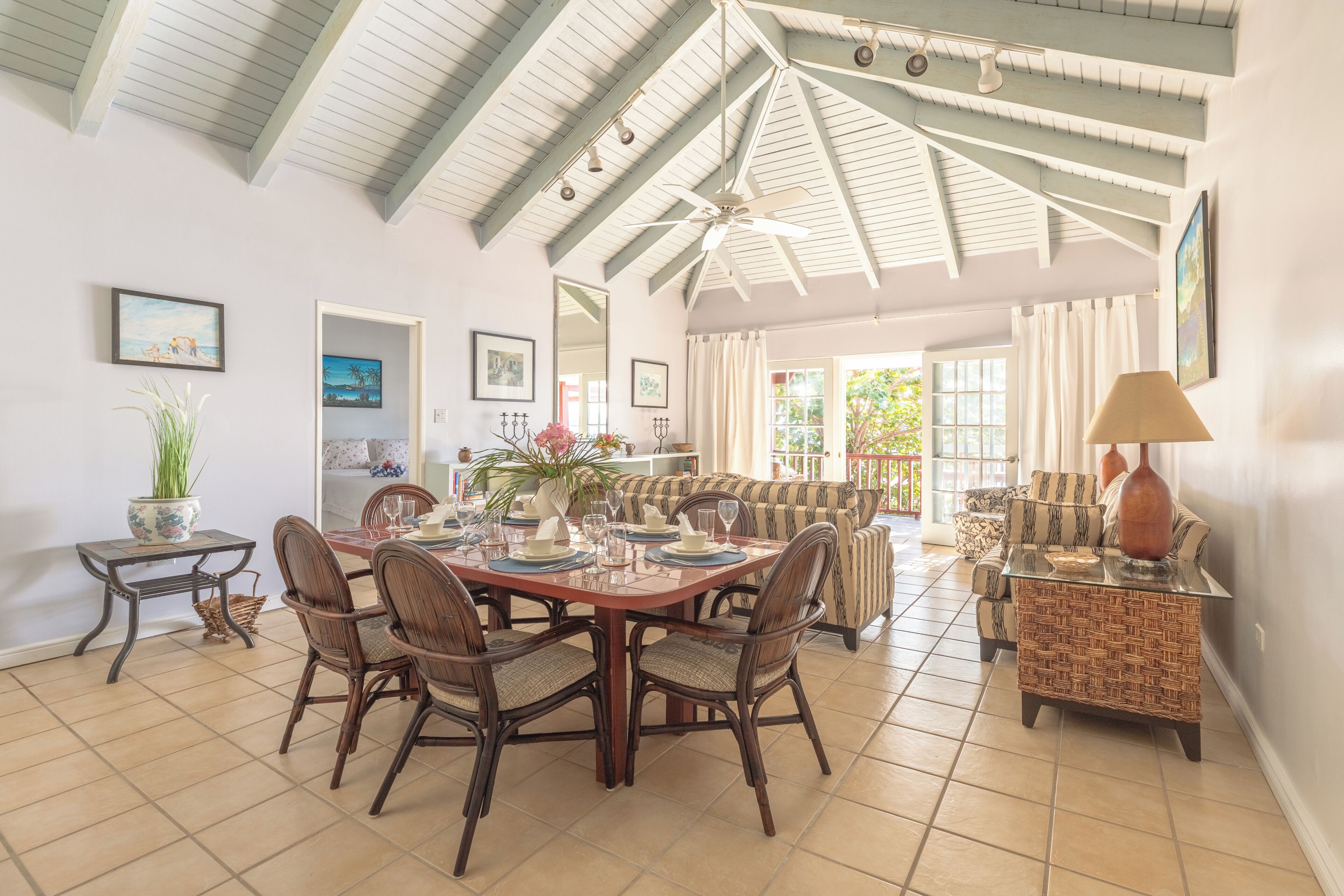 A dining area with a high ceiling, a ceiling fan, and a dining table set for four.
