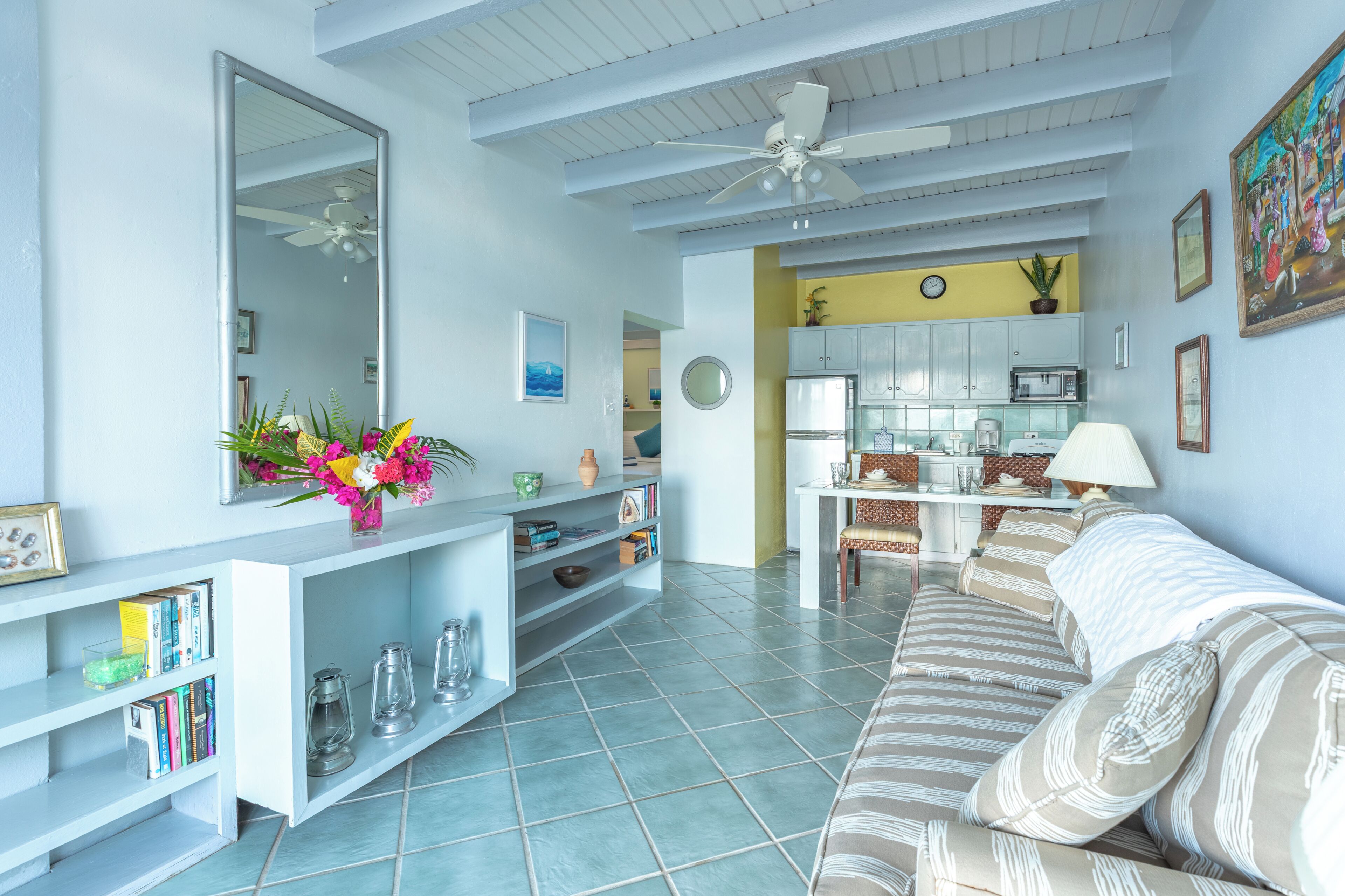 A living room with a sofa, a coffee table, a bookshelf, a dining area, and a kitchen.