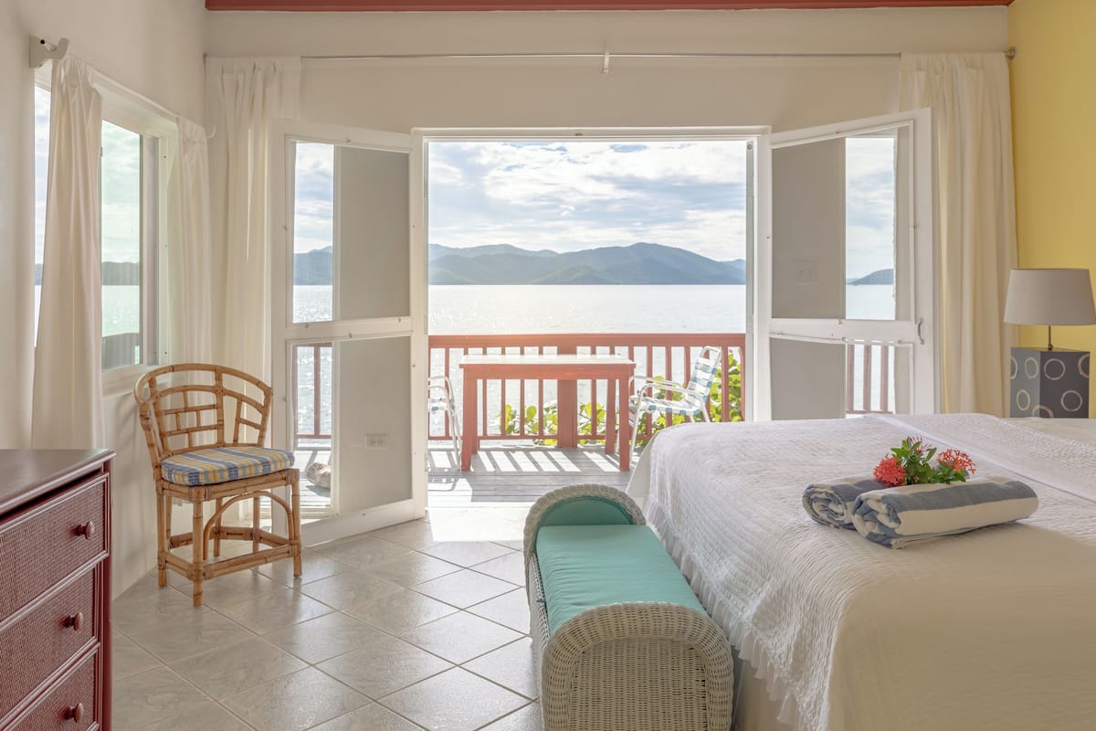 A bedroom with a bed, a chair, a dresser, and a view of a balcony with a railing.