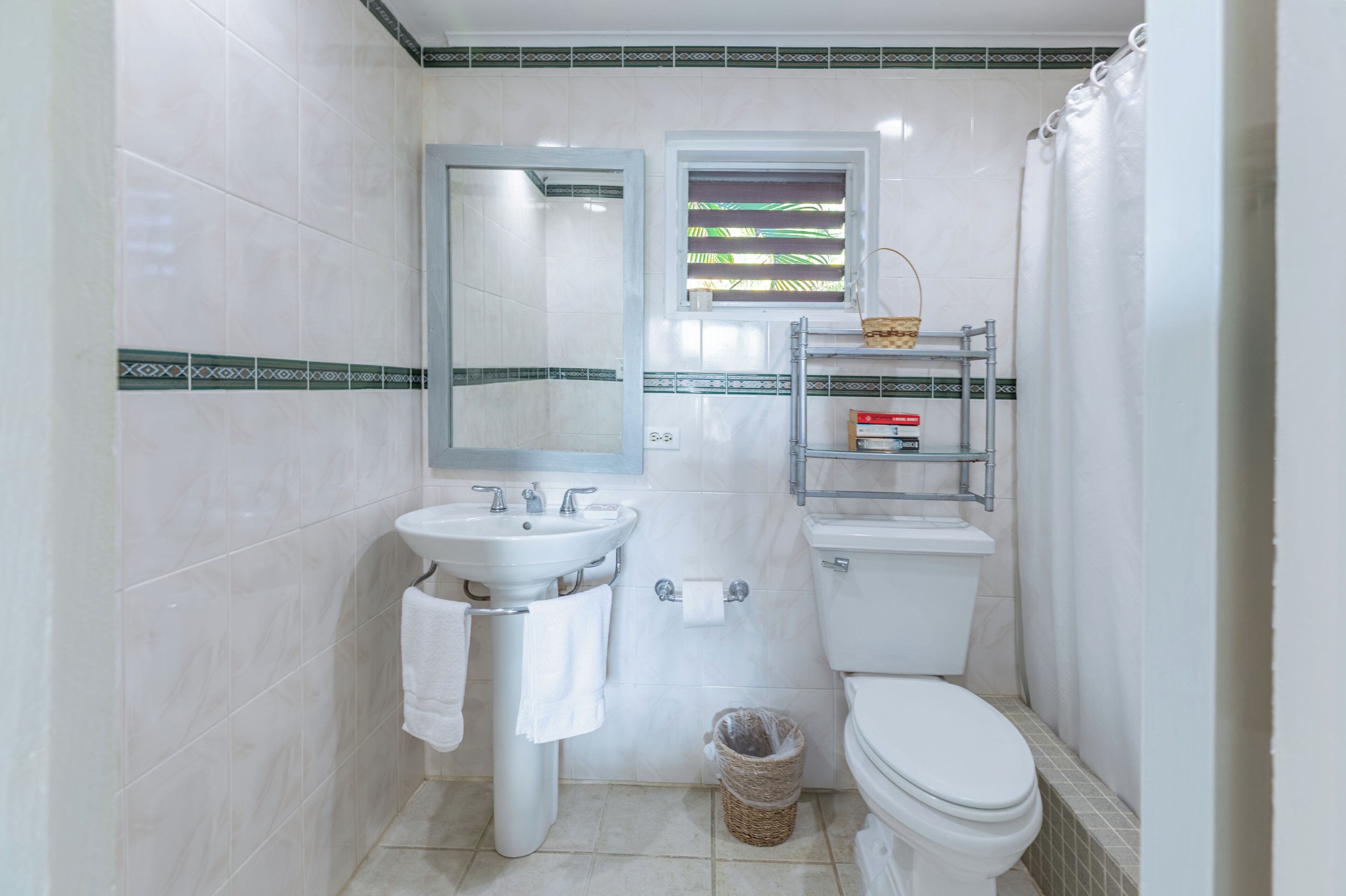 A bathroom with a sink, mirror, toilet, and a small window with a basket on the wall.