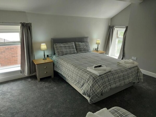 A bedroom with a bed, two bedside tables, a window, and curtains. - Ambrose Hotel (Barrow-in-Furness)