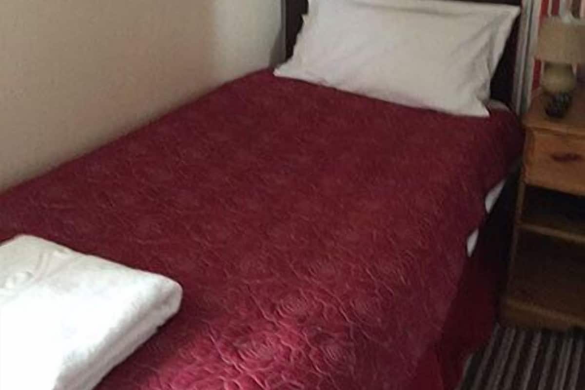 A single bed with a red bedspread and white pillow in a room with striped wallpaper.
