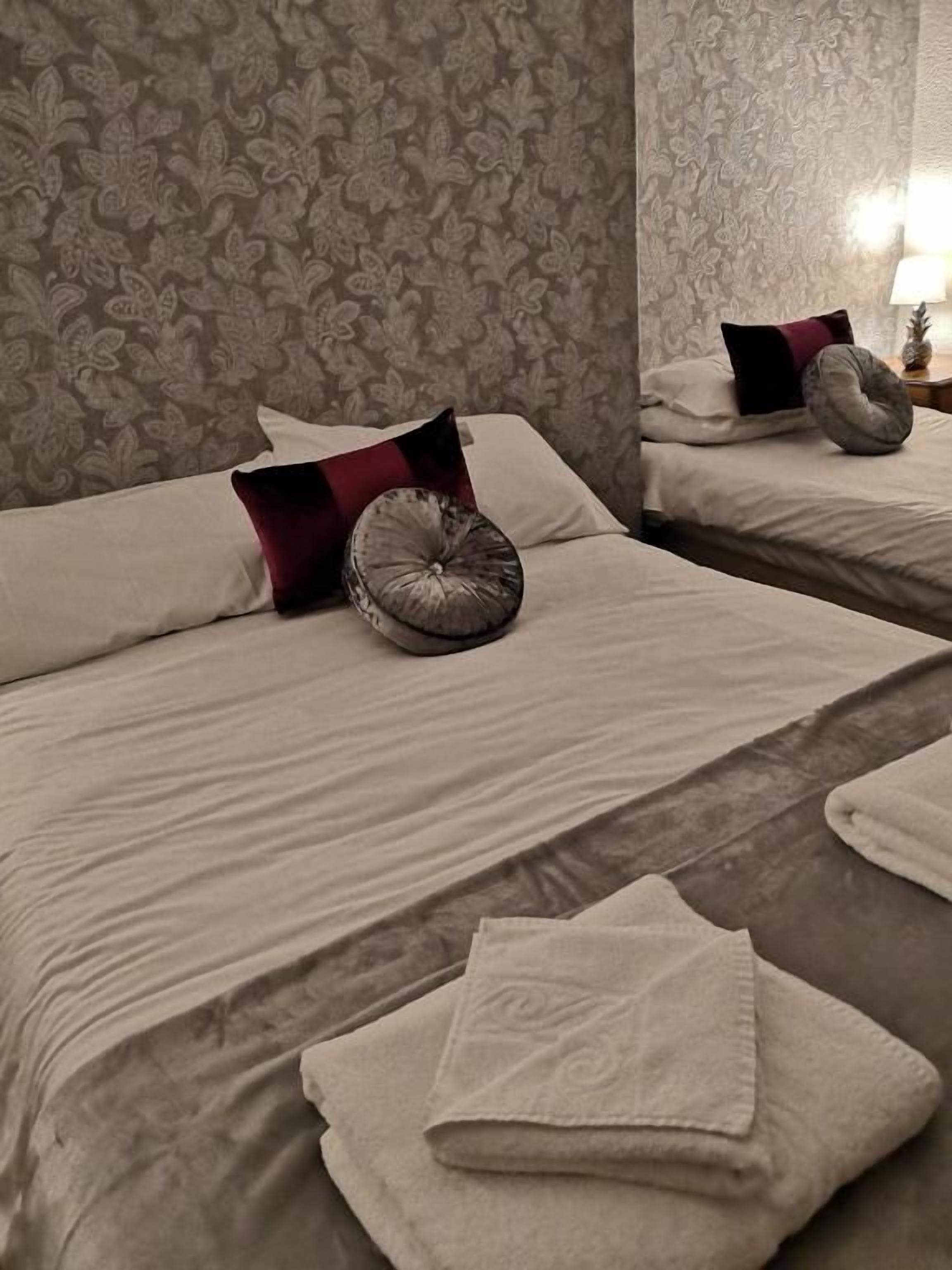 Habitación de hotel con dos camas, cada una con almohada y cojín decorativo. Hay una toalla doblada en el suelo.