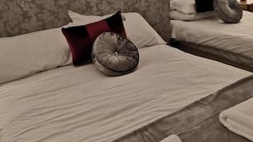 A hotel room with two beds, each with a pillow and a decorative pillow. There is a folded towel on the floor.