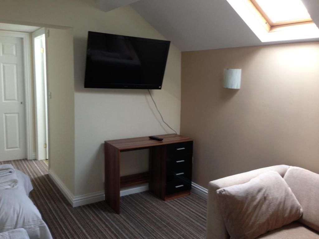 A hotel room with a flat-screen TV mounted on the wall, a wooden desk with drawers, a cushioned chair, and a skylight.