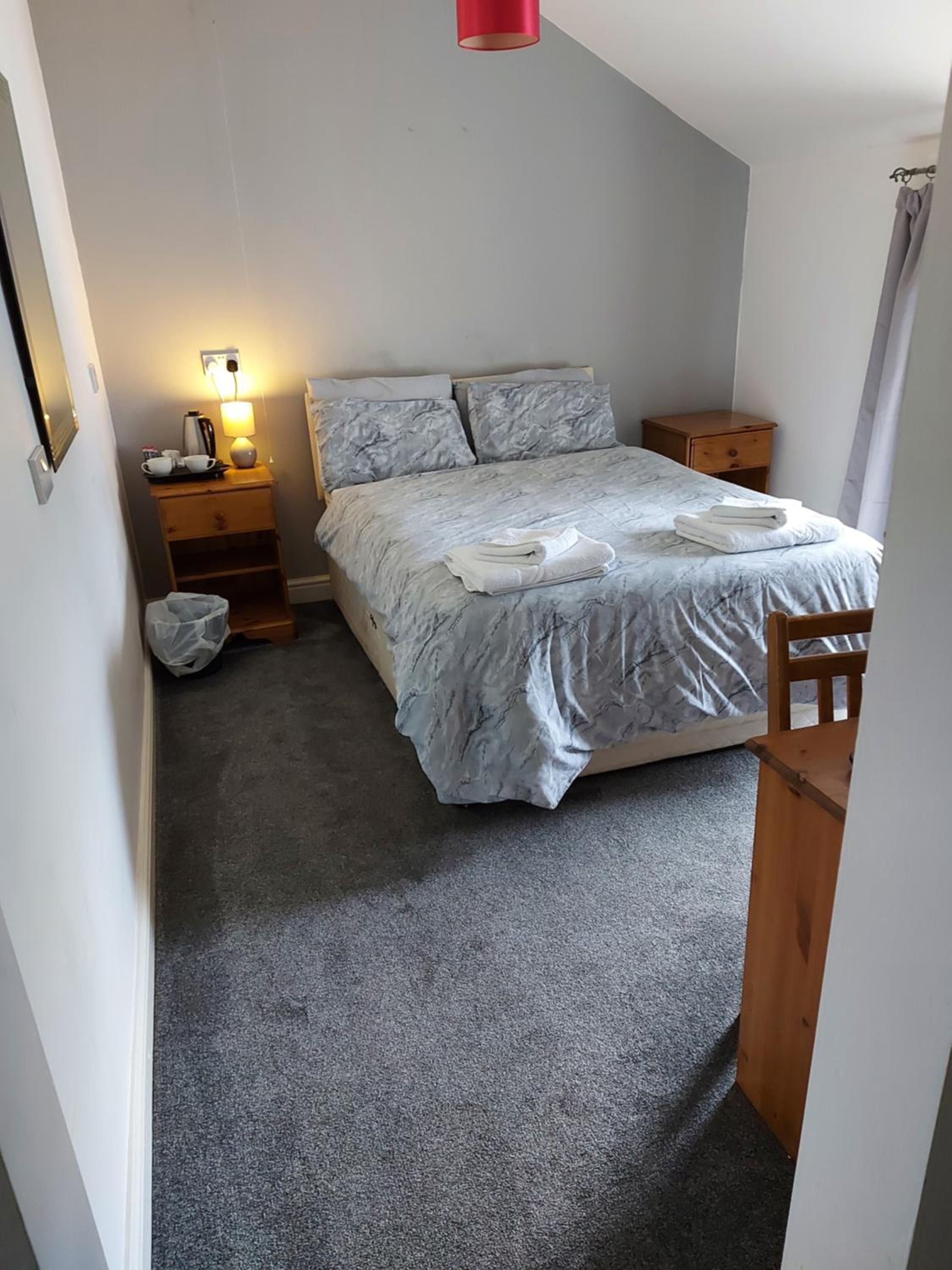 Een kleine, verzorgde slaapkamer met een bed, nachtkastjes, een lamp en een fauteuil.