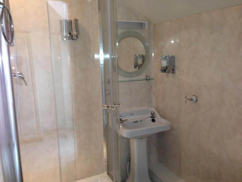 Une salle de bain avec une douche à parois de verre, un lavabo sur colonne et un miroir fixé au mur.