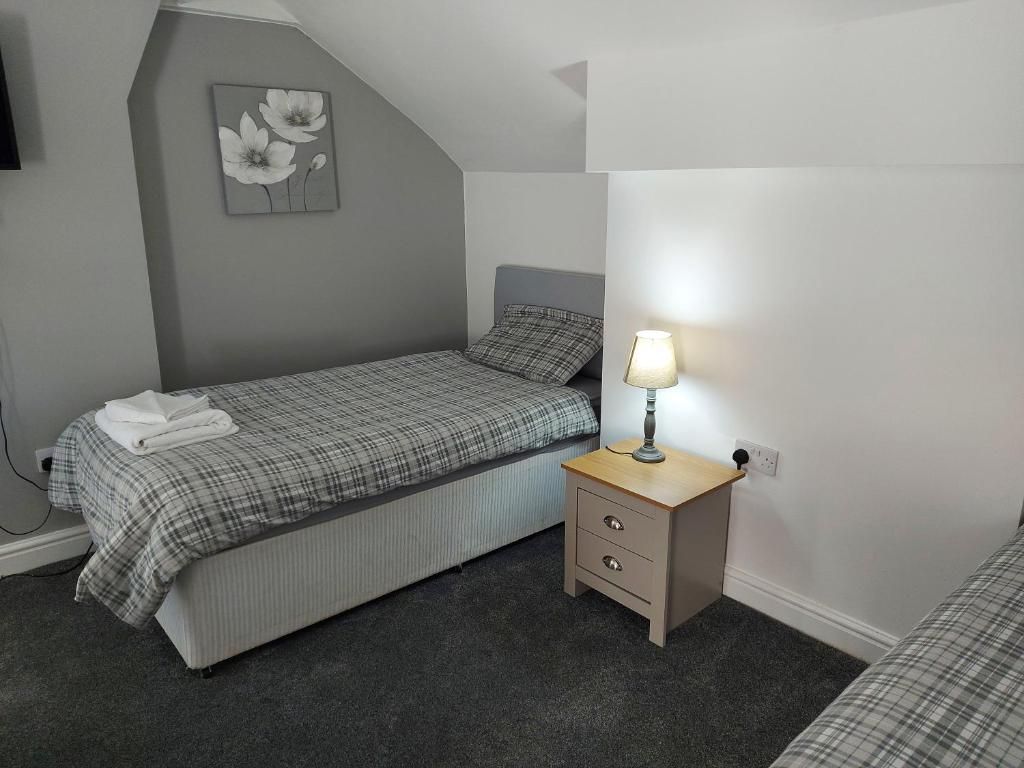 A bedroom with a bed, bedside table, lamp, and a wall-mounted artwork.