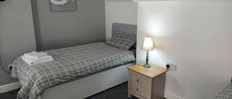 A bedroom with a bed, bedside table, lamp, and a wall-mounted artwork.