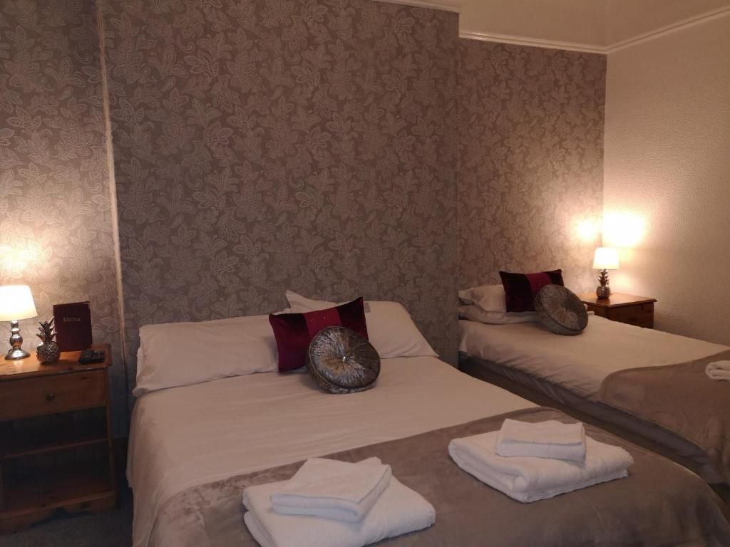 Une chambre d’hôtel avec deux lits, une table de chevet avec une lampe et un mur orné d’un motif floral.