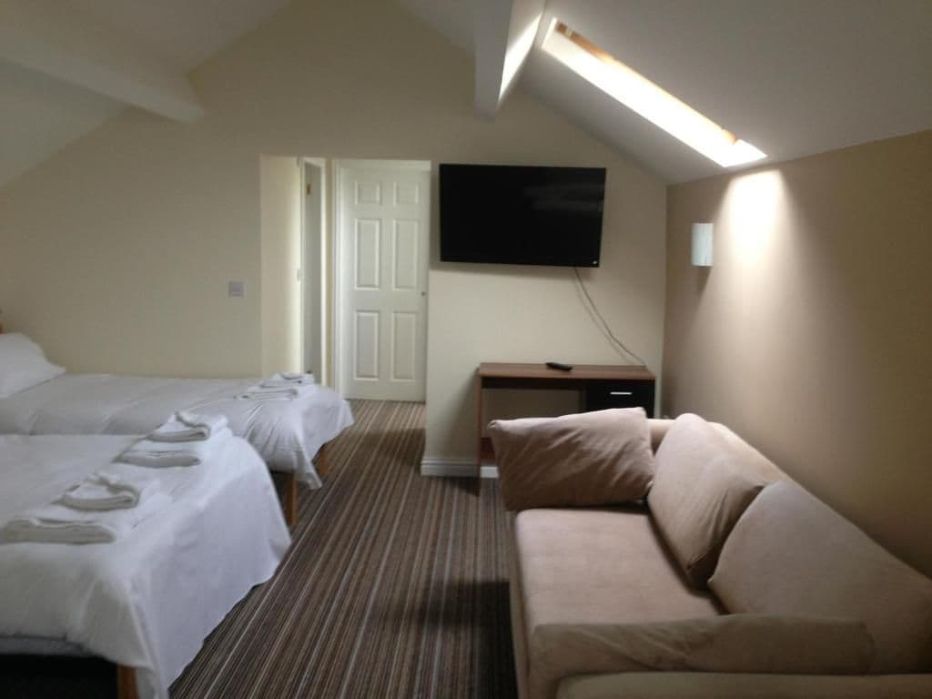 A hotel room with two beds, a sofa, a television, and a desk.