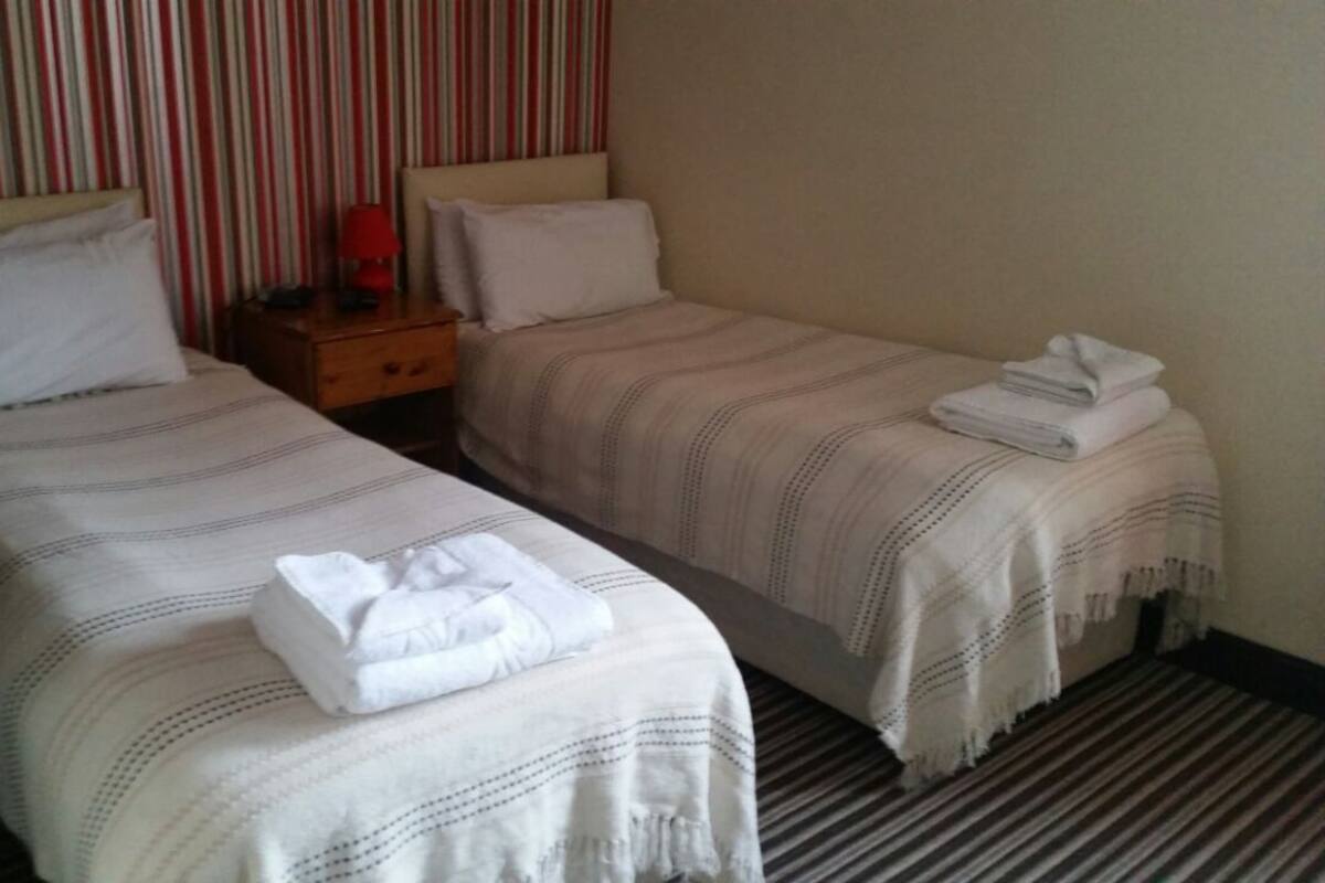 Two single beds with striped bedding, a nightstand with a lamp, and a folded towel on the right bed.