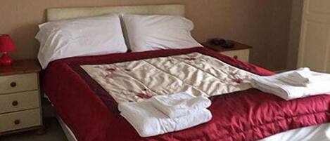 Un lit bien fait, avec une literie blanche et rouge, une table de chevet avec une lampe et une petite table de nuit avec un téléphone.