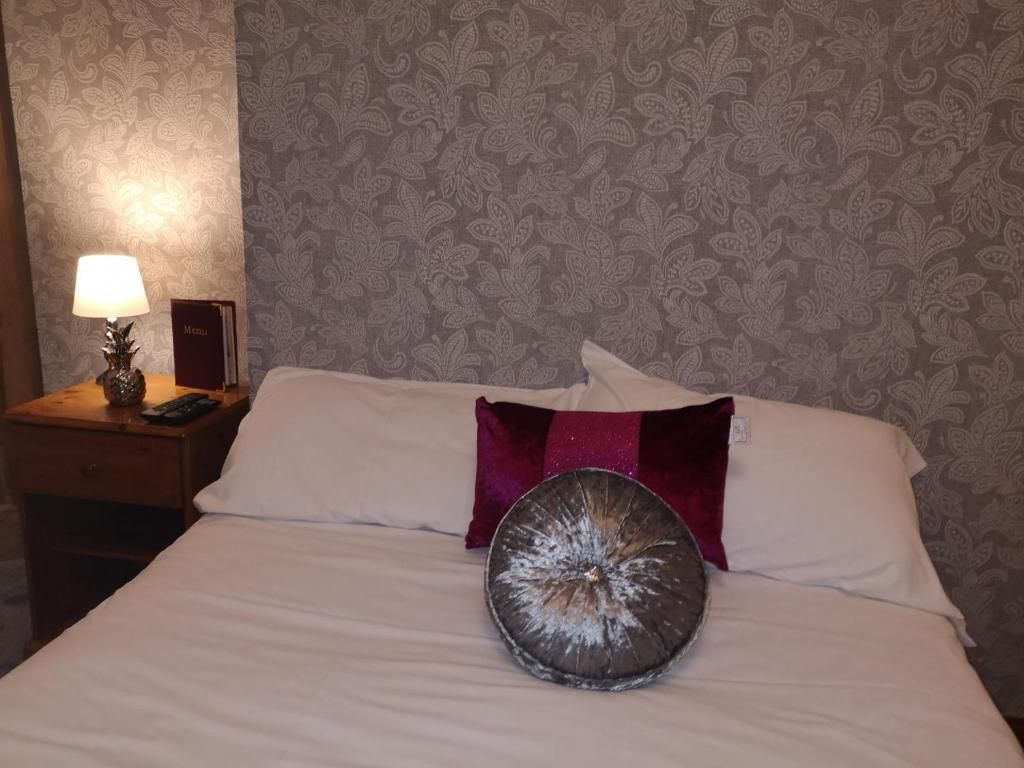 A bed with a white comforter, a round decorative pillow, a red accent pillow, and a nightstand with a lamp and a menu sign.