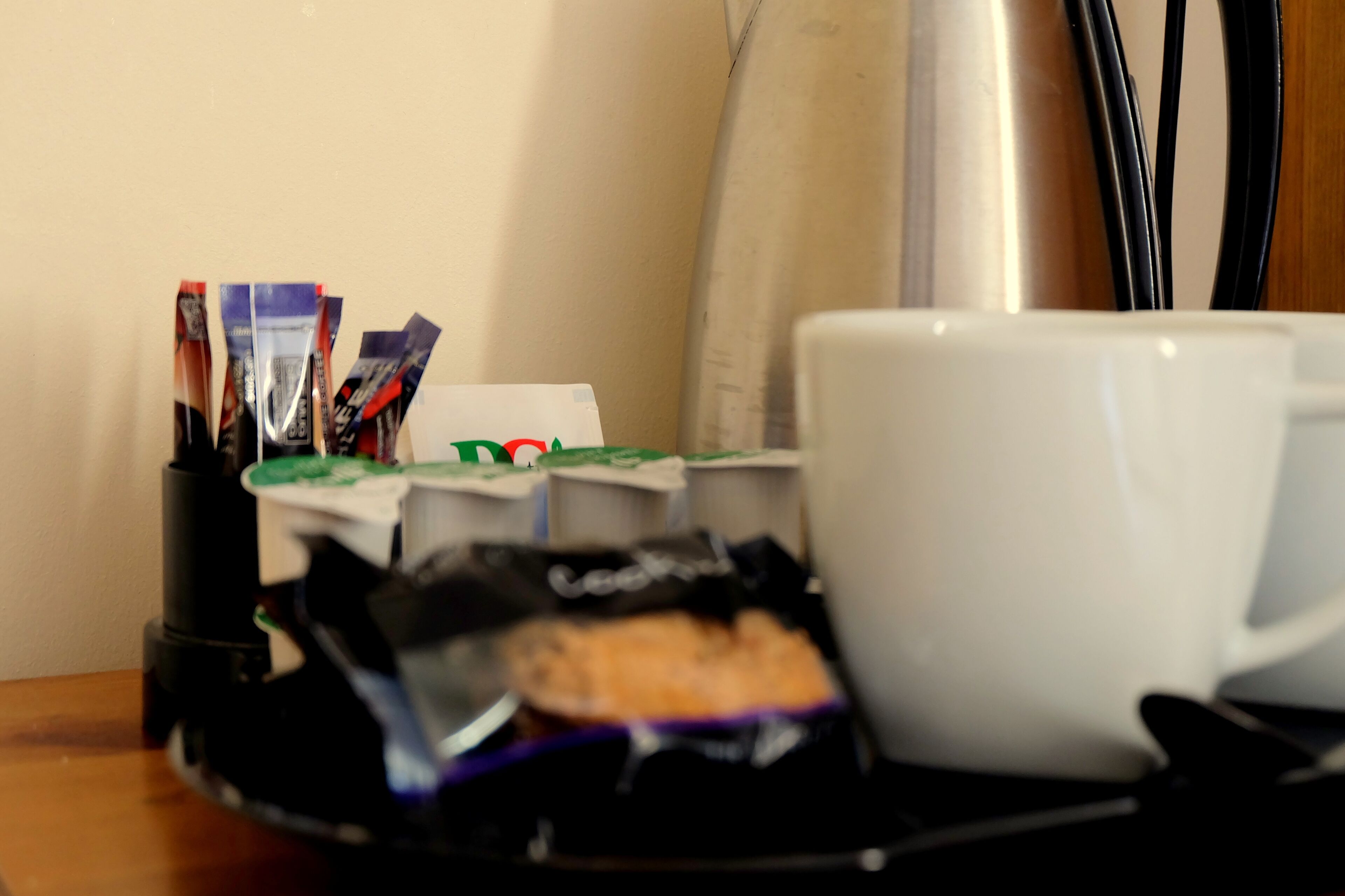 A white cup on a tray with a packet of cookies and a pen holder with pens.
