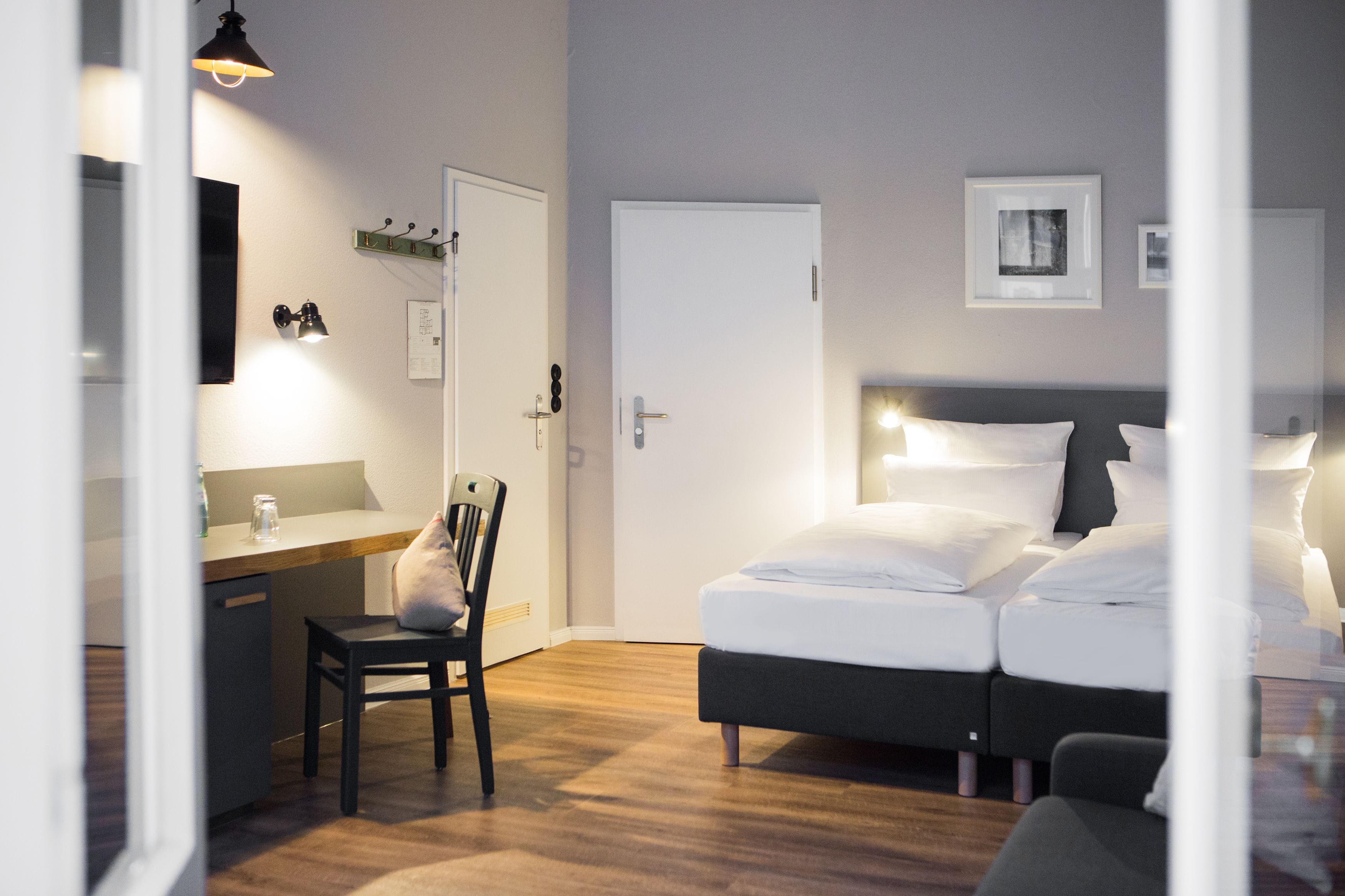 A modern hotel room with a bed, bedside table, chair, and a desk with a chair.