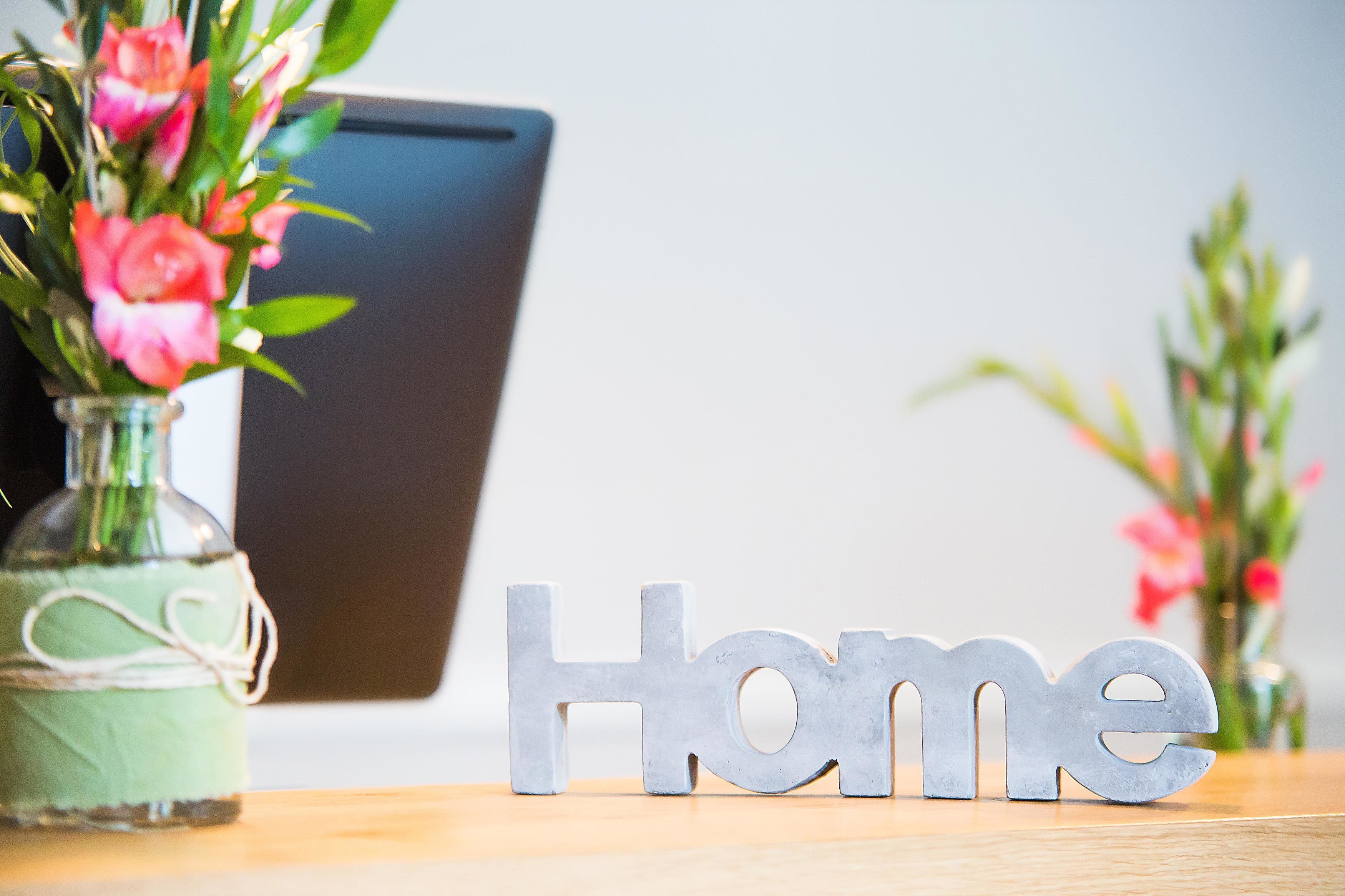 Un tavolo in legno con un vaso di fiori rosa e un cartello metallico con la scritta 'Home'.