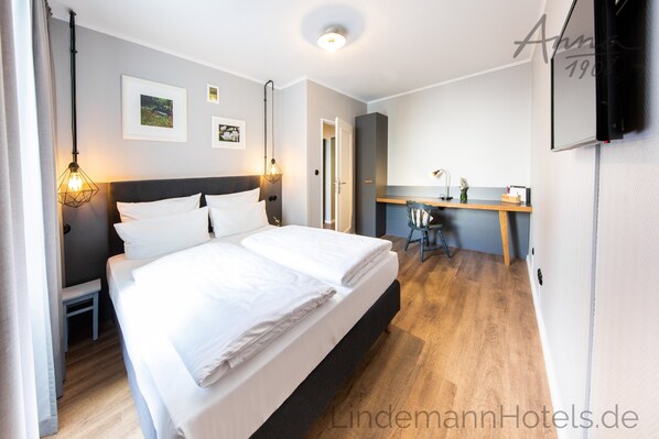 A modern hotel room with a large bed, bedside tables, a desk, and a chair.