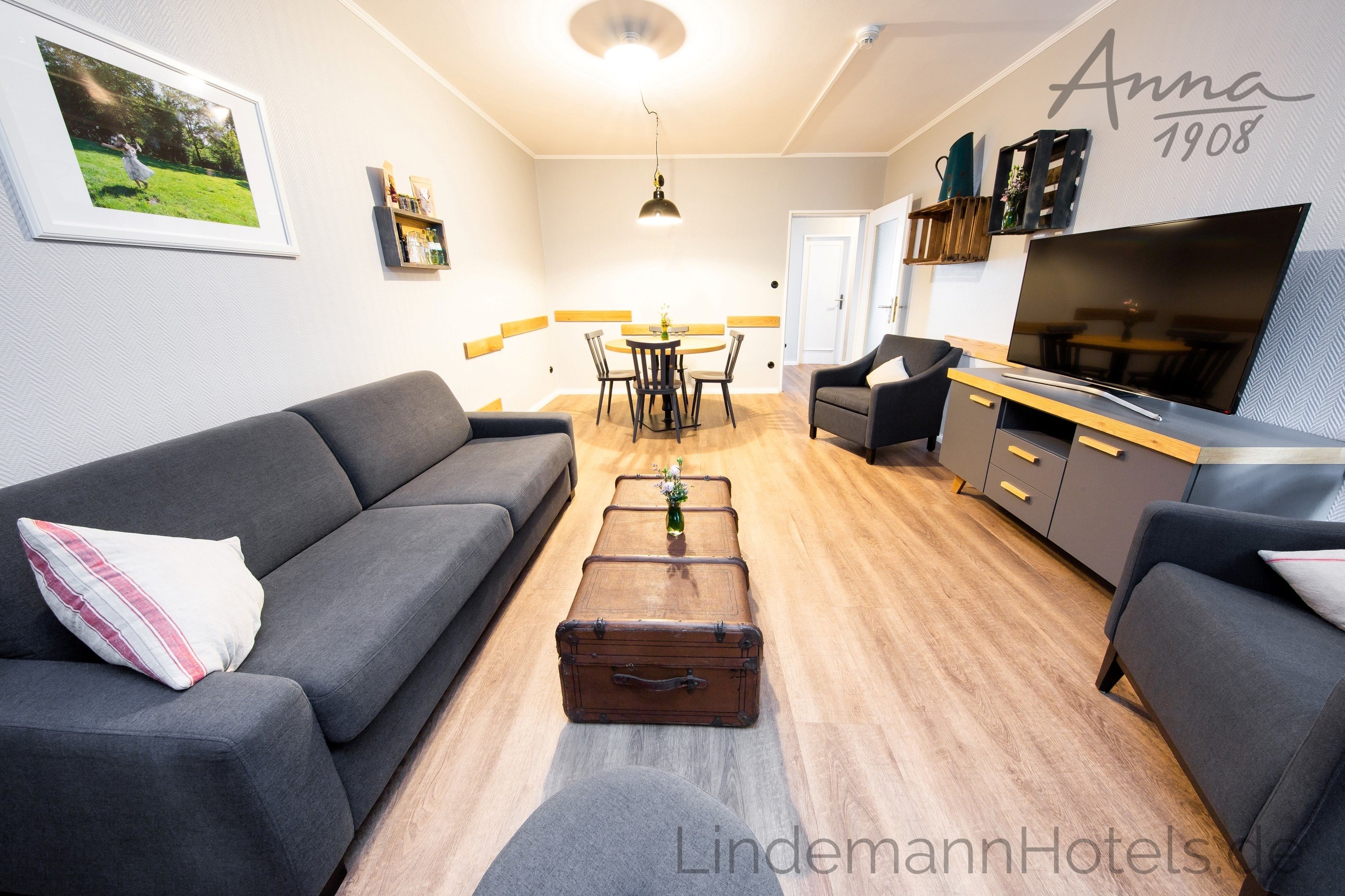 A modern living room with a grey sofa, a wooden coffee table, and a dining area with a round table and chairs.