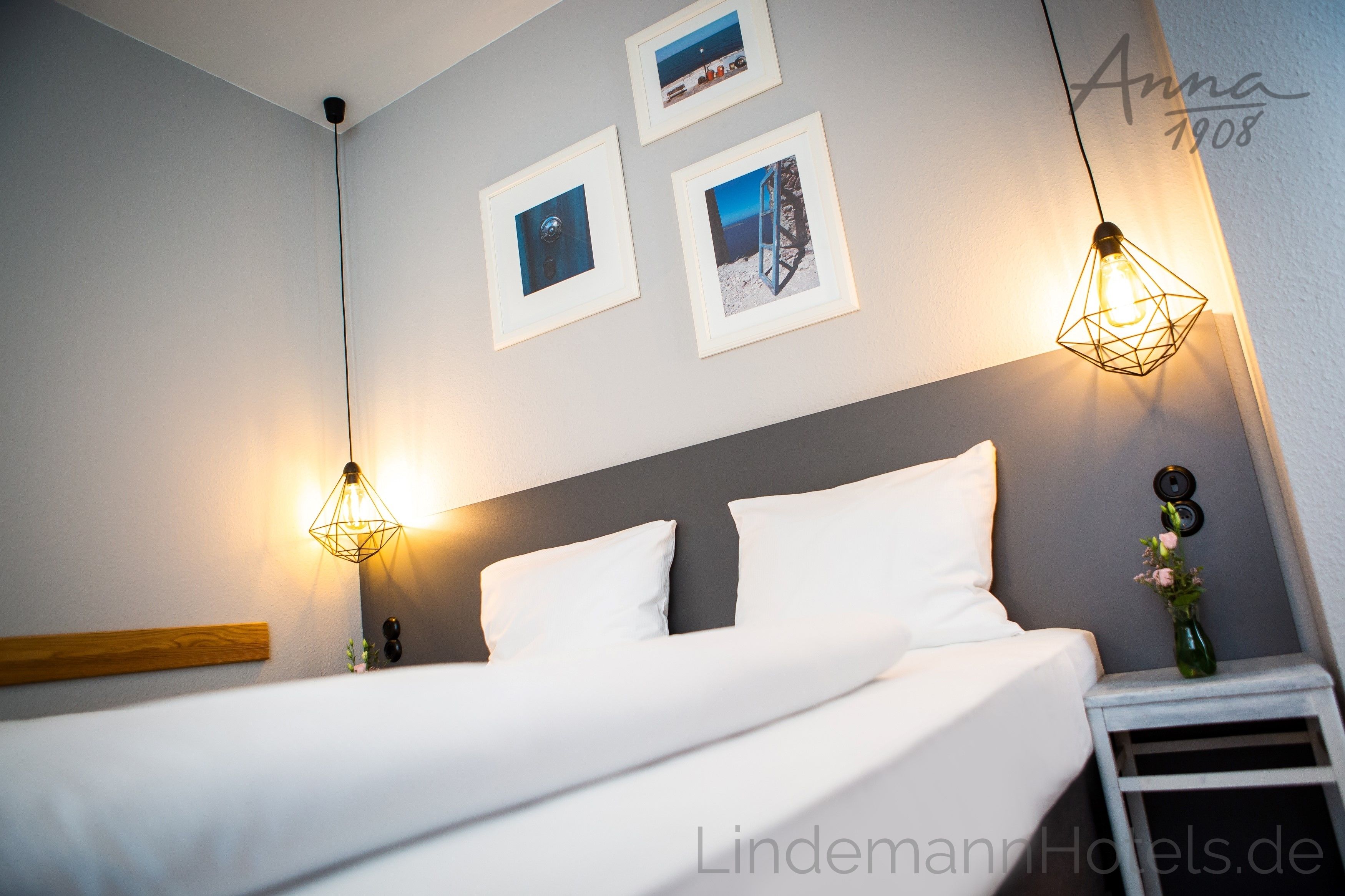 A neatly made bed with white linens, a grey headboard, and two wall-mounted light fixtures.