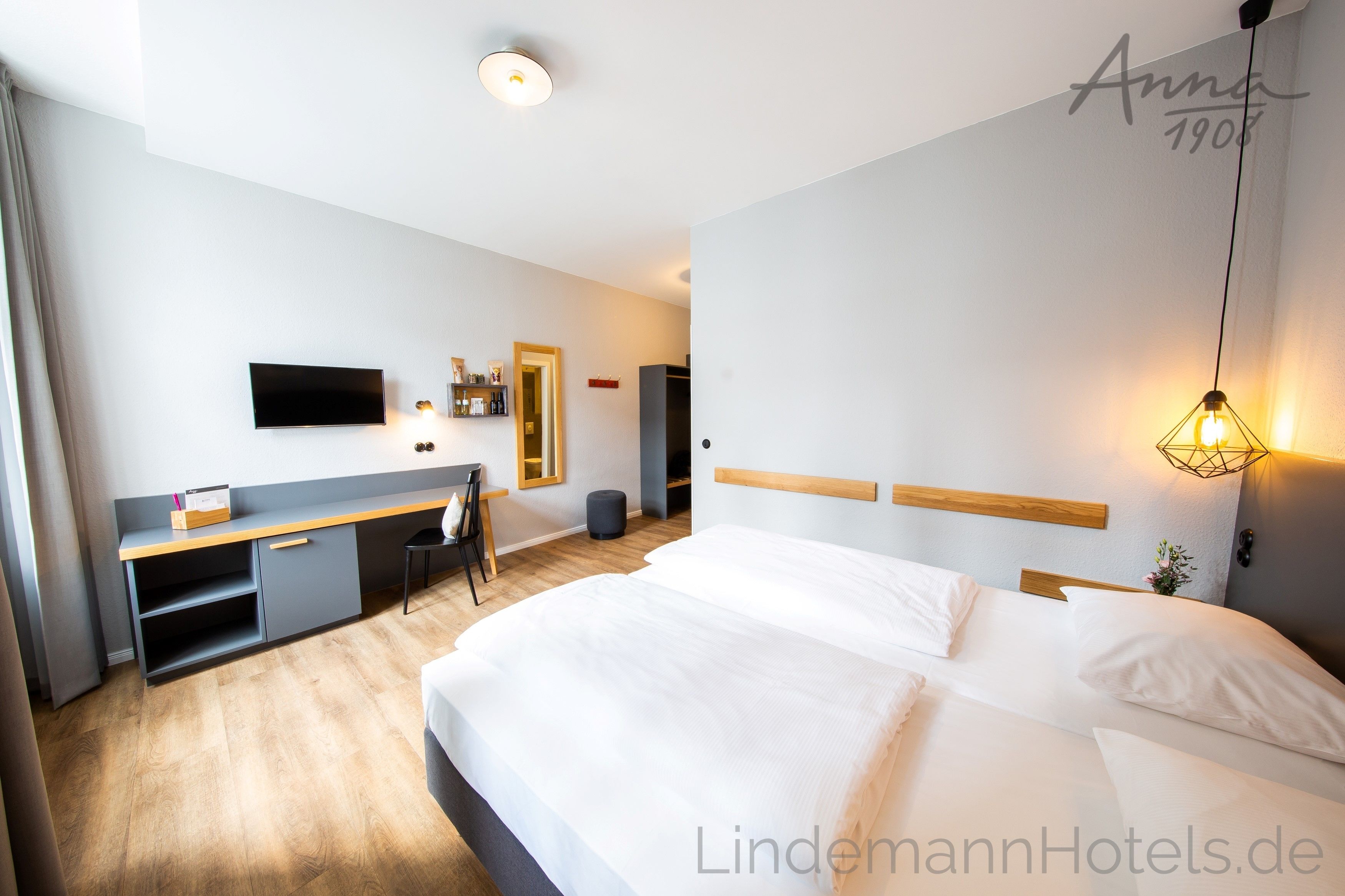 A hotel room with a bed, a desk, a chair, a TV, and a mirror.