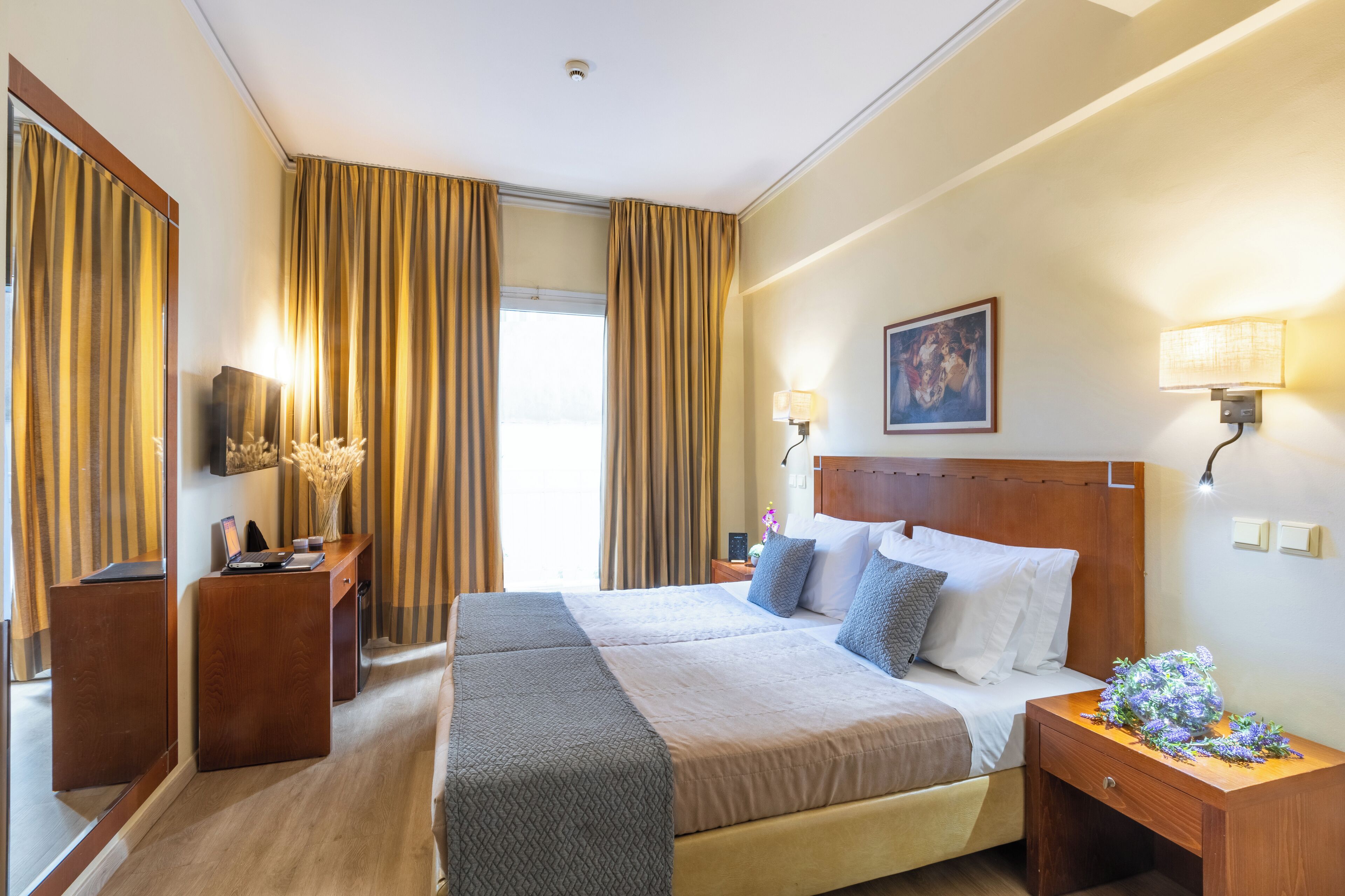 Habitación de hotel con una cama grande, un escritorio, una silla, un espejo, una lámpara y una ventana con cortinas.