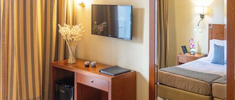 Une chambre d’hôtel avec un lit, un bureau avec une télévision, un miroir et une fenêtre avec des rideaux.