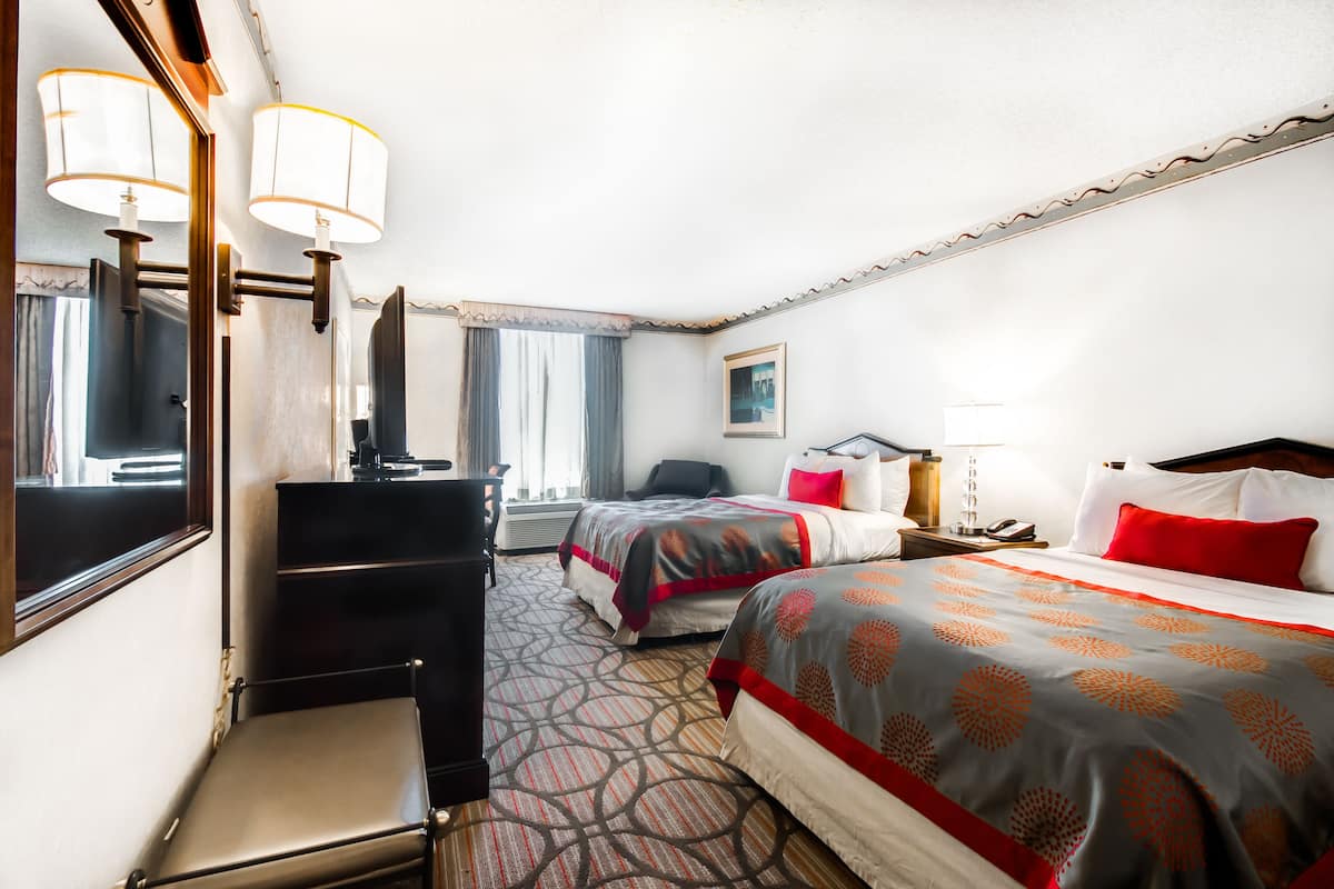 A hotel room with two beds, a desk, a chair, a dresser, and a large mirror.