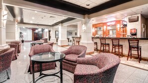 A spacious lobby with patterned armchairs, a glass coffee table, and a bar area with wooden chairs.