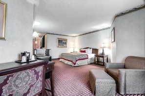 Quarto de hotel com cama, escrivaninha, cadeira, sofá e televisão.